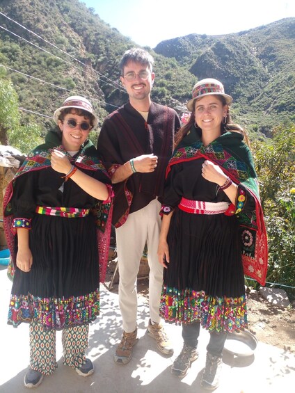 Three people in traditional attire standing outdoors with a mountainous landscape in the background. 2