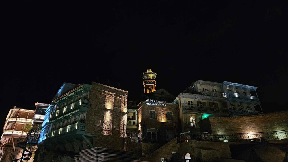 A night view of a historic town with illuminated buildings, including the Khokhobi Hotel. 3