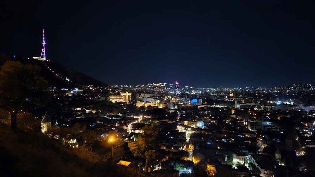 A nighttime cityscape with illuminated buildings and a prominent tower on a hill. 1