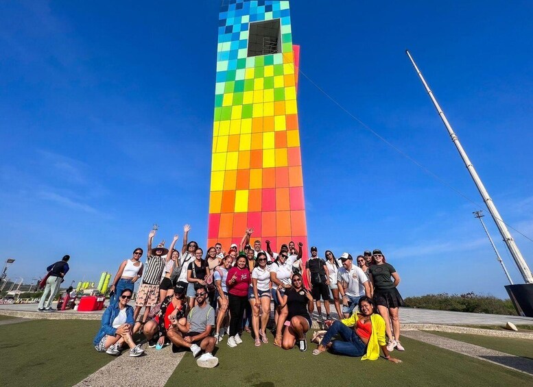 A group of people posing in front of a tall, colorful tower with a clear blue sky in the background. 3