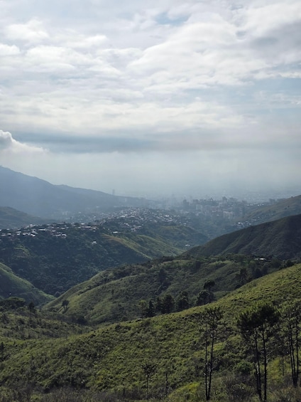 A valley with a city in the distance, surrounded by green hills and a cloudy sky. 2