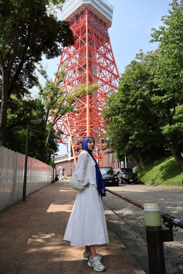 A person standing on a sidewalk with a tall red tower in the background. 3