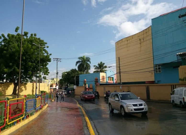 A street with cars parked on the side, a pedestrian crossing, and buildings with colorful facades. 4