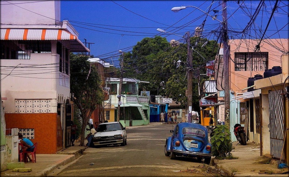 A narrow urban street with parked cars, buildings, and overhead power lines. 3