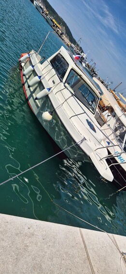 A white boat docked at a marina with clear blue water and a hilly landscape in the background. 2