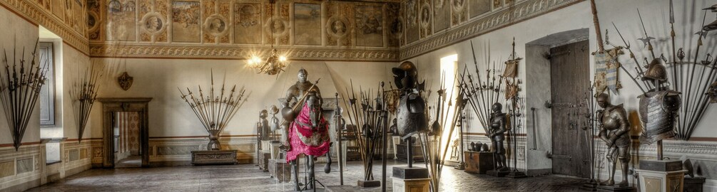 A grand hall with ornate ceilings, a central statue, and an array of medieval armor and weapons. 2