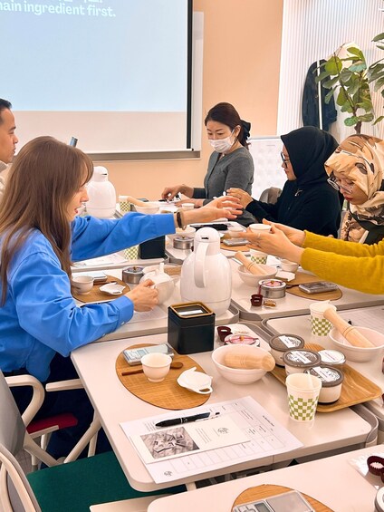 A group of people seated around a table with various kitchen utensils and containers, engaged in a cooking or baking activity. 4