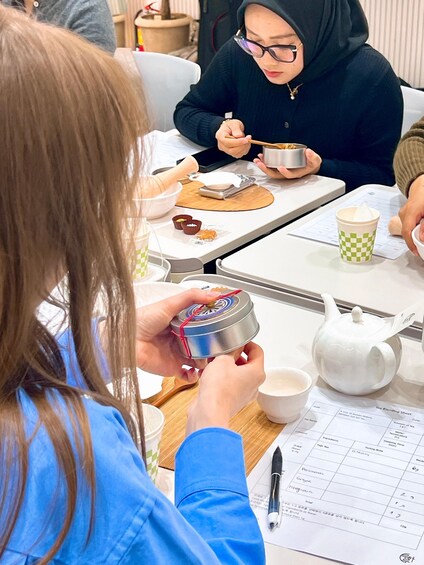 A person holding a small metal container, possibly a tea pot, with a lid and a red cord. 3