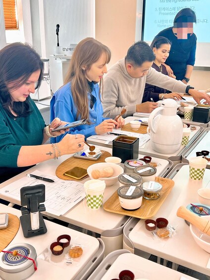 A group of people engaged in a cooking class, with ingredients and utensils on the table. 2
