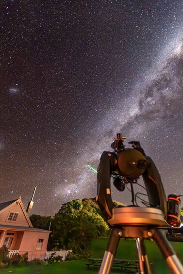 A telescope aimed at a starry sky with the Milky Way visible, set against a house and trees. 4