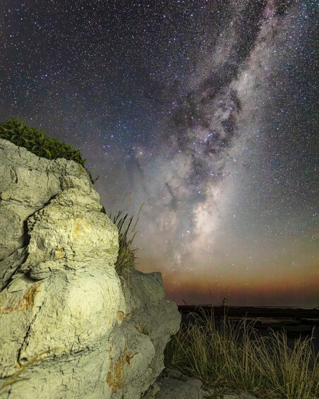 A rocky cliff with grass, a starry night sky, and the Milky Way. 2