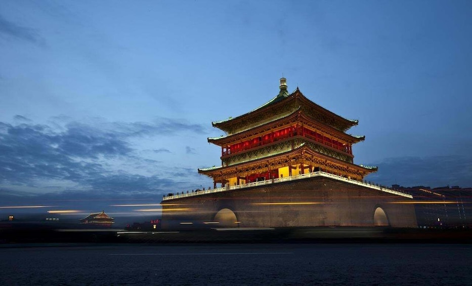 A traditional Chinese pagoda at dusk with illuminated red lanterns, a stone bridge, and a river in the foreground. 4