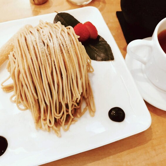 A plate of noodles with a cherry and a black dot, and a cup of tea on the side. 2
