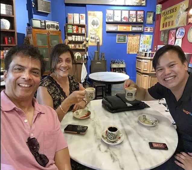 Three people sitting at a table with cups of coffee, surrounded by various items and decorations. 3