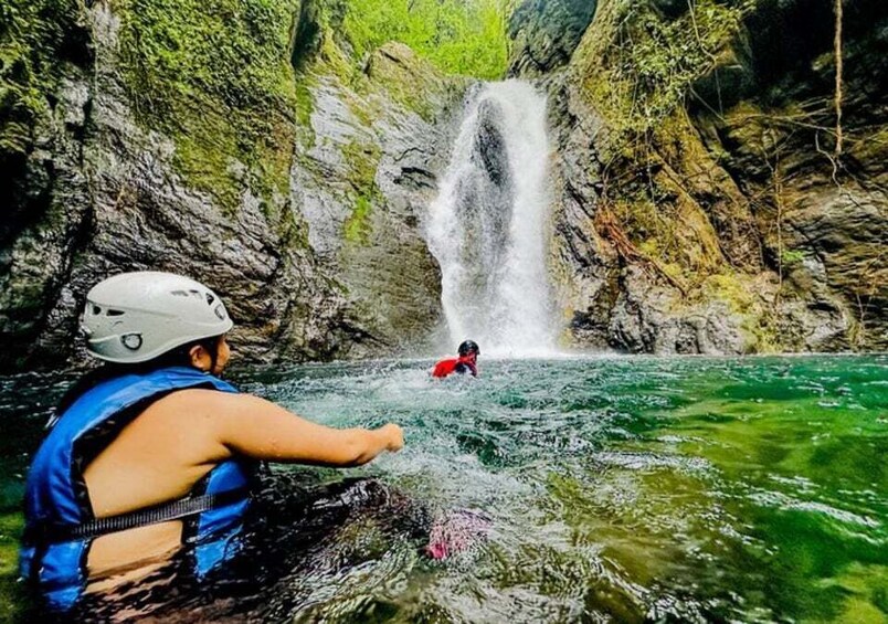 A person in a blue life jacket paddling a kayak towards a waterfall in a rocky gorge. 1