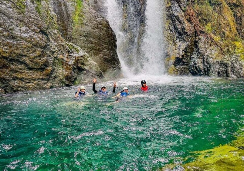 A group of people swimming in a clear river with a waterfall in the background. 5