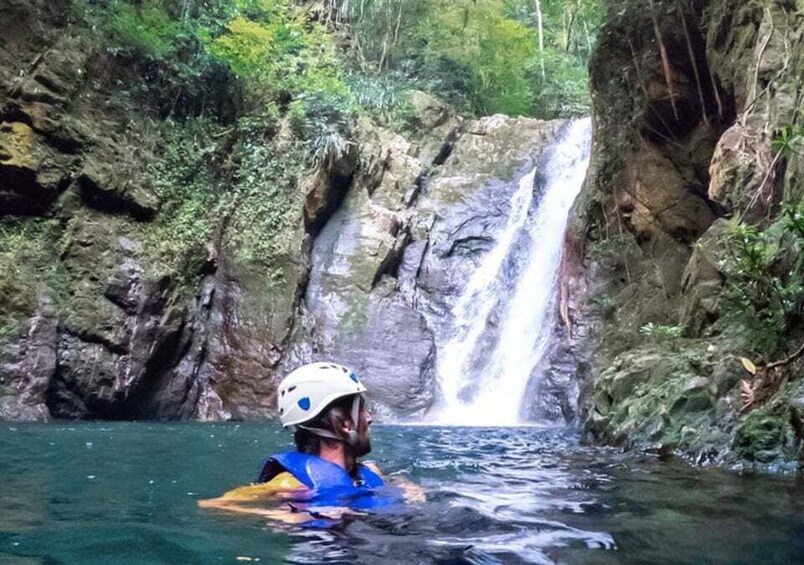 A kayaker in a helmet and life jacket paddling through a river with a waterfall in the background. 4