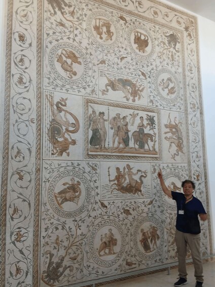 A person standing in front of a detailed wall with classical artwork. 3