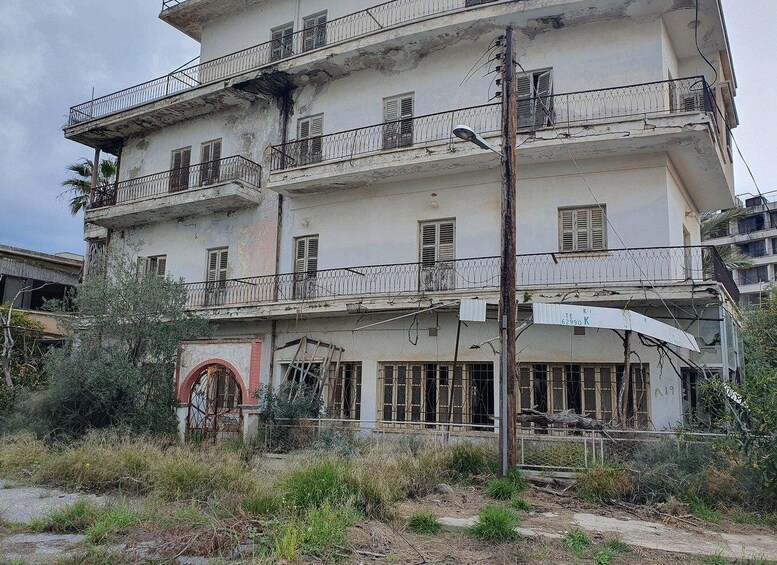 A multi-story building with balconies, a damaged facade, and overgrown vegetation. 2