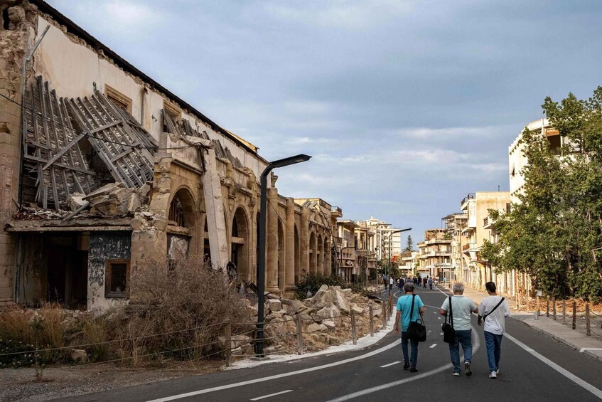 A street with dilapidated buildings, a clear sky, and pedestrians walking. 4