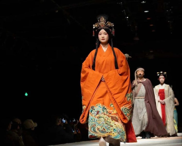 A person in traditional orange attire walking on a stage. 2