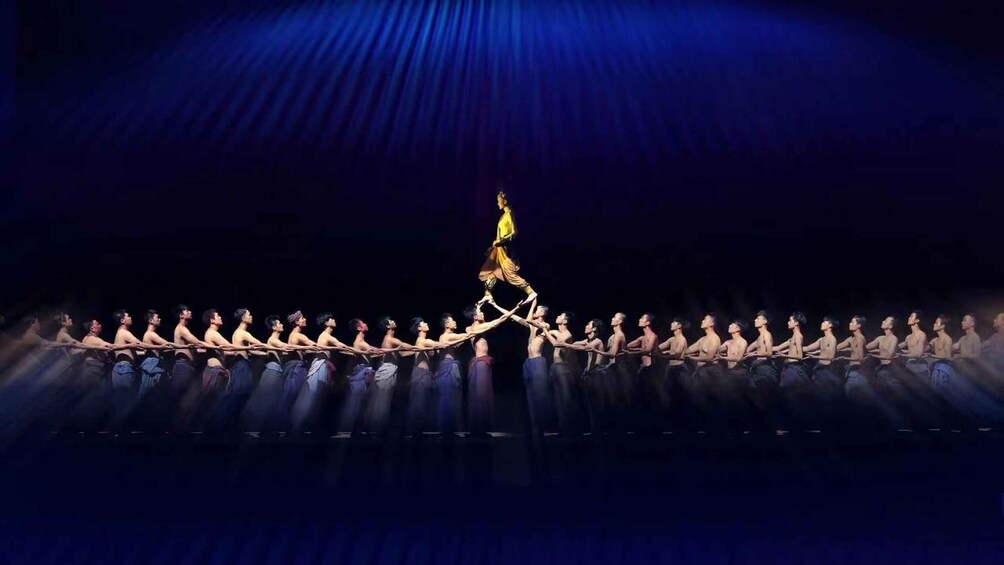 A group of dancers in a line formation on a stage with a spotlight effect. 1