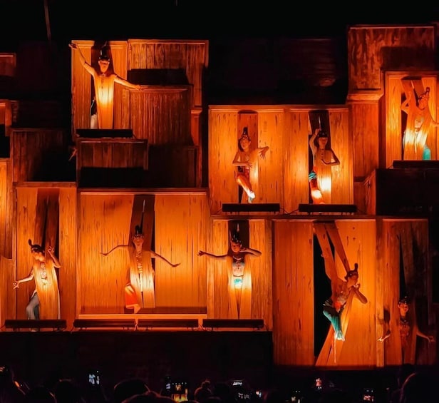 A stage with performers in dynamic poses, illuminated by warm lighting, surrounded by wooden structures. 4