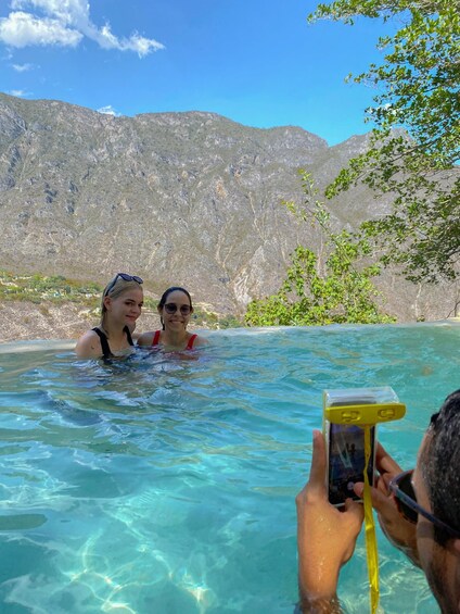 Two people in a clear pool with mountains in the background. 5