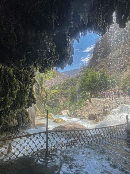A cave entrance with a waterfall, a rope barrier, and a rocky landscape. 3