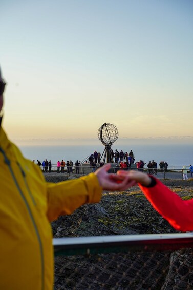 A person in a yellow jacket extending their hand towards a spherical structure with a wireframe design, with a group of people in the background. 2