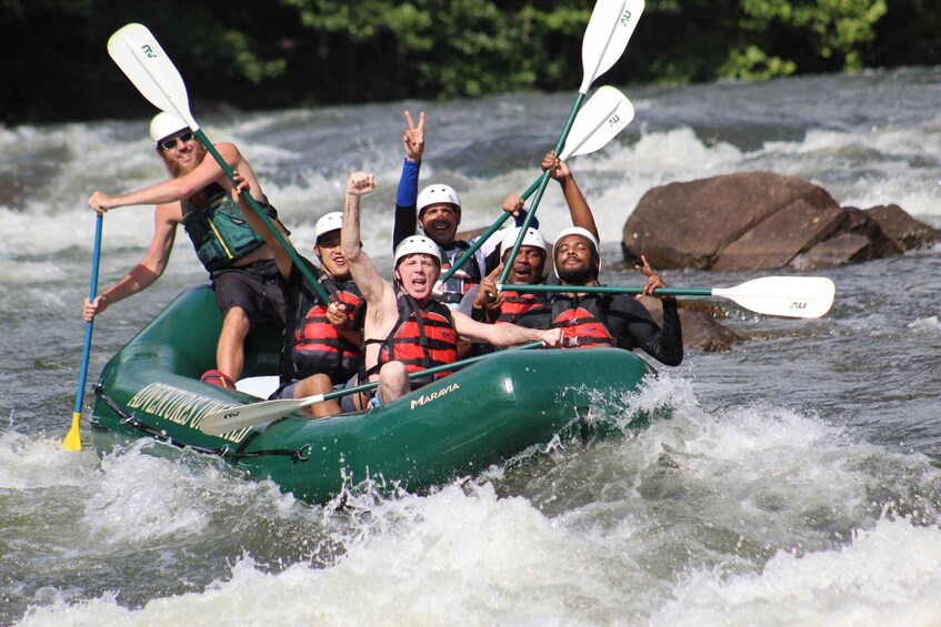 A group of people in a green inflatable raft navigating a river with rapids. 4