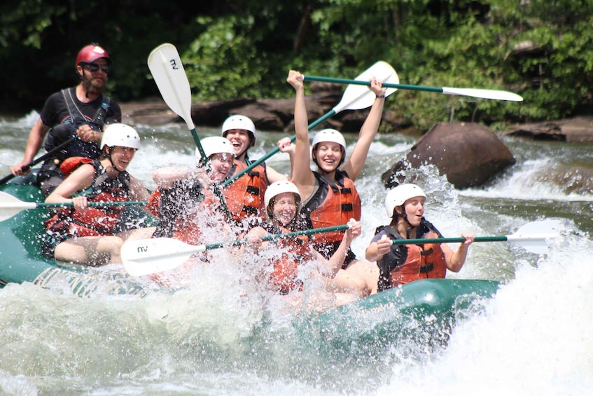 A group of people in a green raft navigating a river with white paddles. 3