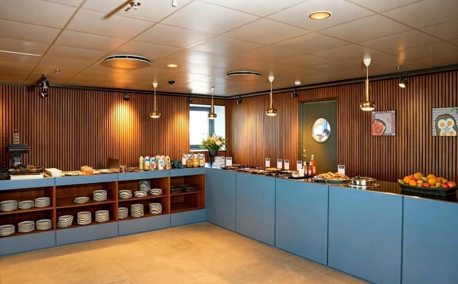 A buffet counter with food items, a clock, and a window with blinds. 3