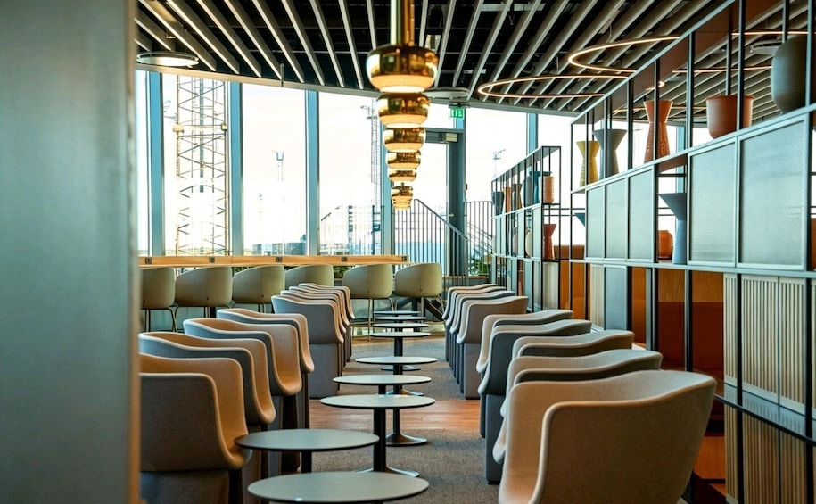 A modern interior with rows of chairs and tables, large windows, and a metal ceiling structure. 1