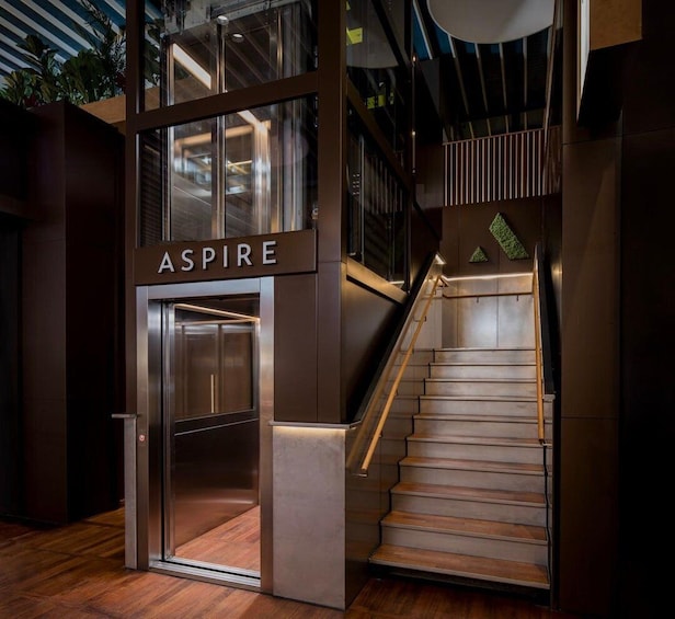 A modern elevator with 'ASPIRE' signage, a wooden staircase, and a glass elevator door. 4