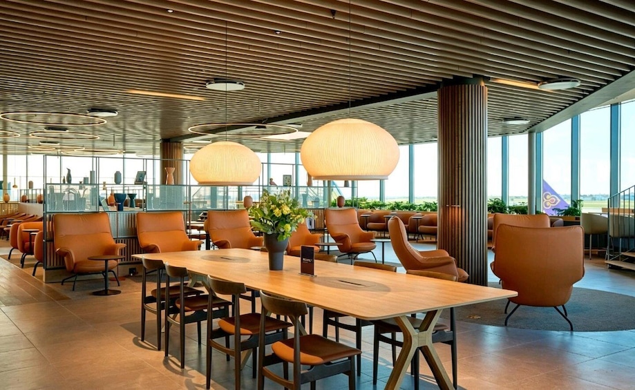 A modern indoor space with a long wooden table, orange chairs, and large hanging lamps. 5