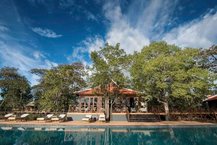 A pool with lounge chairs, a wooden gazebo, and trees. 5