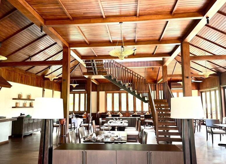 A spacious restaurant with wooden beams, a staircase, and tables set for dining. 4