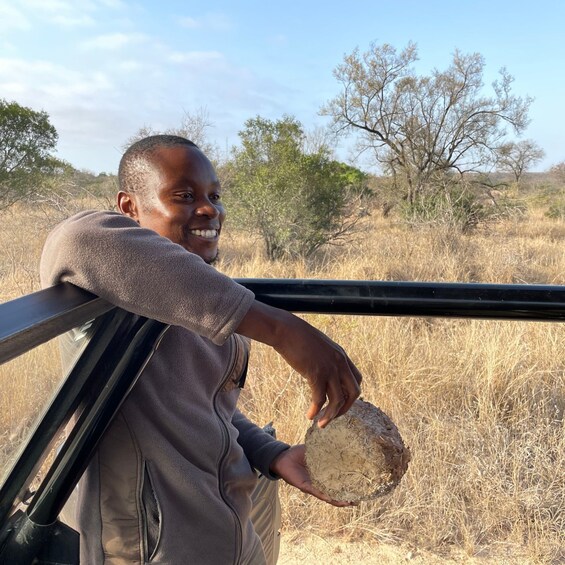 A person holding a rock inside a vehicle, with dry grass and trees in the background. 5