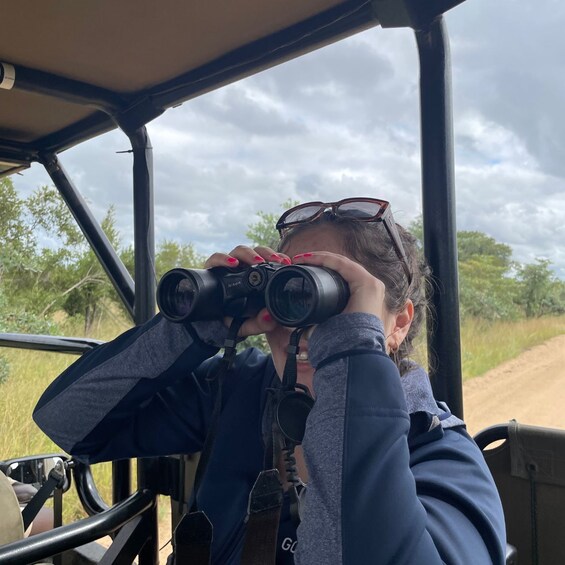 A person using binoculars inside a vehicle, with a natural landscape visible through the window. 4