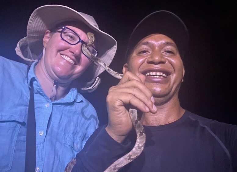 Two people, one wearing a blue shirt and a hat, and the other holding a snake. 3
