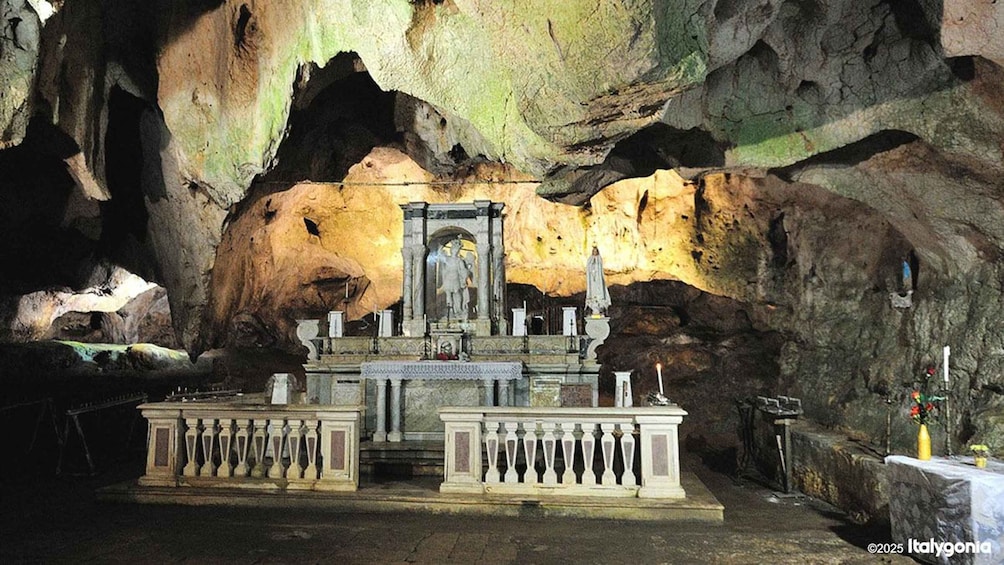 A cave interior with a central statue, stone benches, and a candle holder. 4