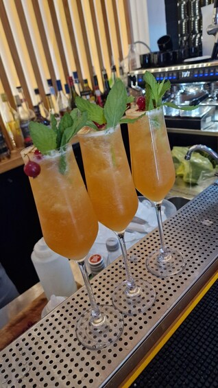 Two cocktails garnished with mint leaves and cherries, placed on a bar counter with a perforated tray. 1