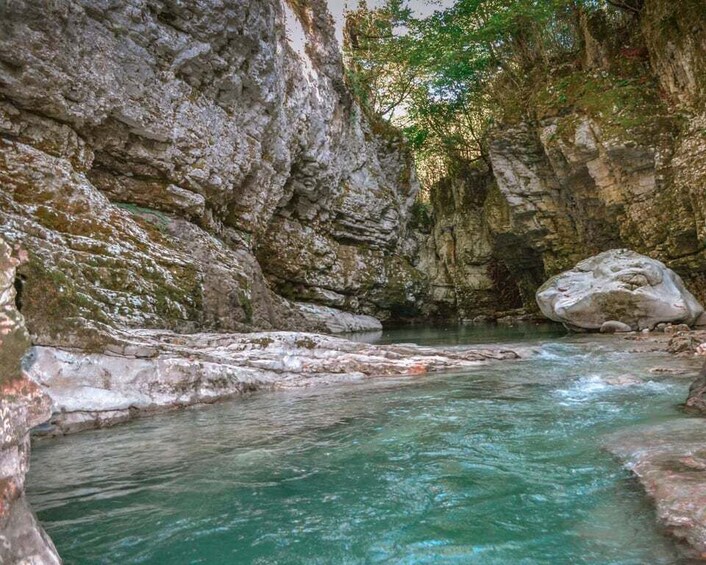 A clear turquoise river flowing through a rocky gorge with large boulders and dense foliage. 3