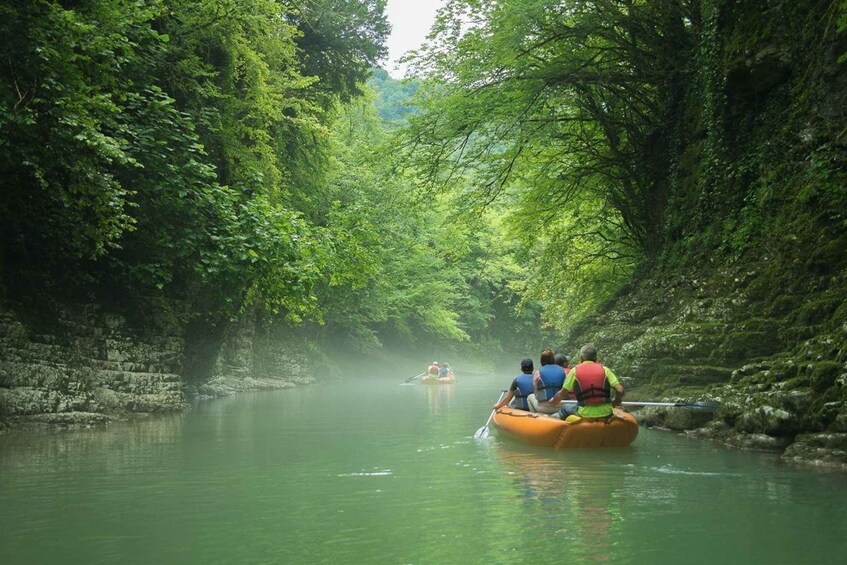 A river surrounded by dense green foliage, with people in a raft and a motorboat. 5