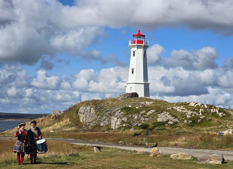 A white lighthouse with a red top on a grassy hill by the sea. 4