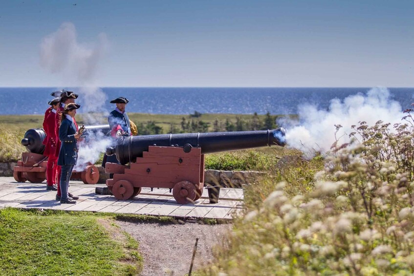 A historical reenactment with individuals in period costumes and a cannon firing on a coastal path. 1
