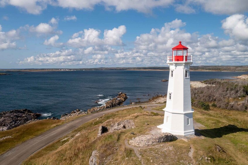 A white lighthouse with a red top on a grassy cliff overlooking a body of water. 5