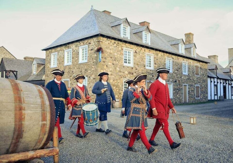 A historical reenactment group in period costumes marching in front of a stone building with a traditional roof. 2