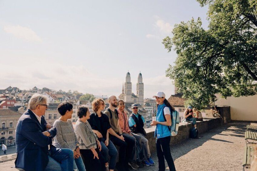 A group of people sitting on a rooftop terrace overlooking a cityscape with historic buildings. 3